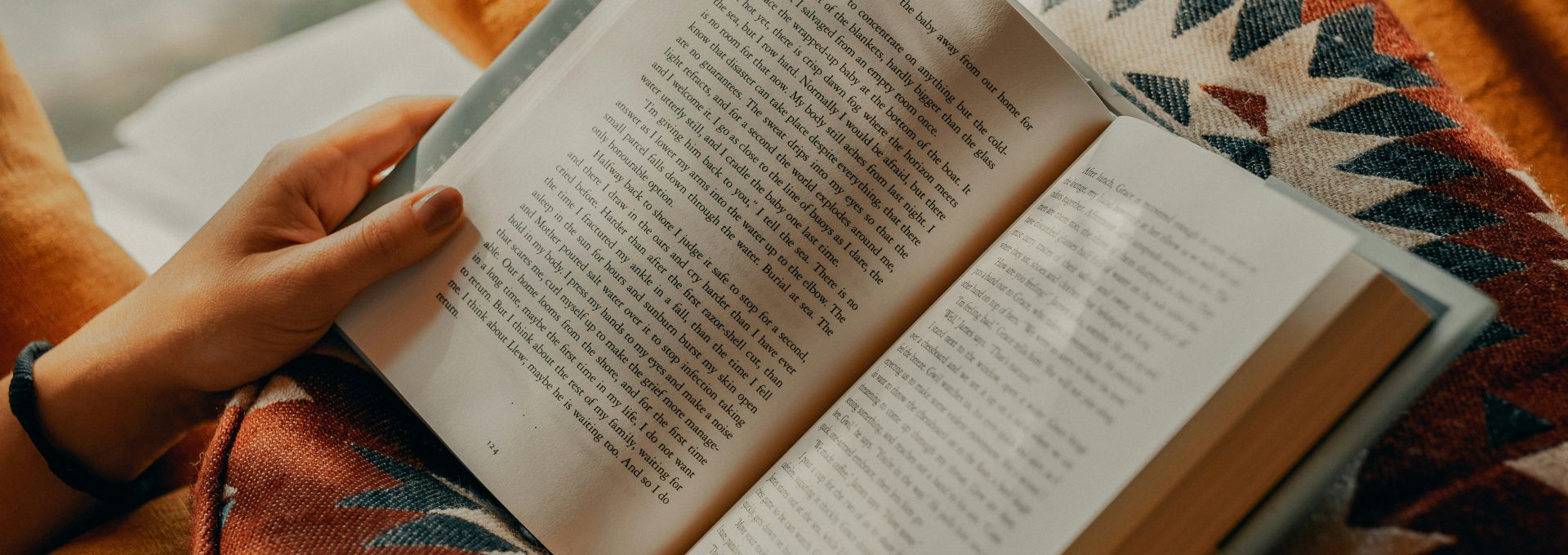 person reading book on brown and beige textile